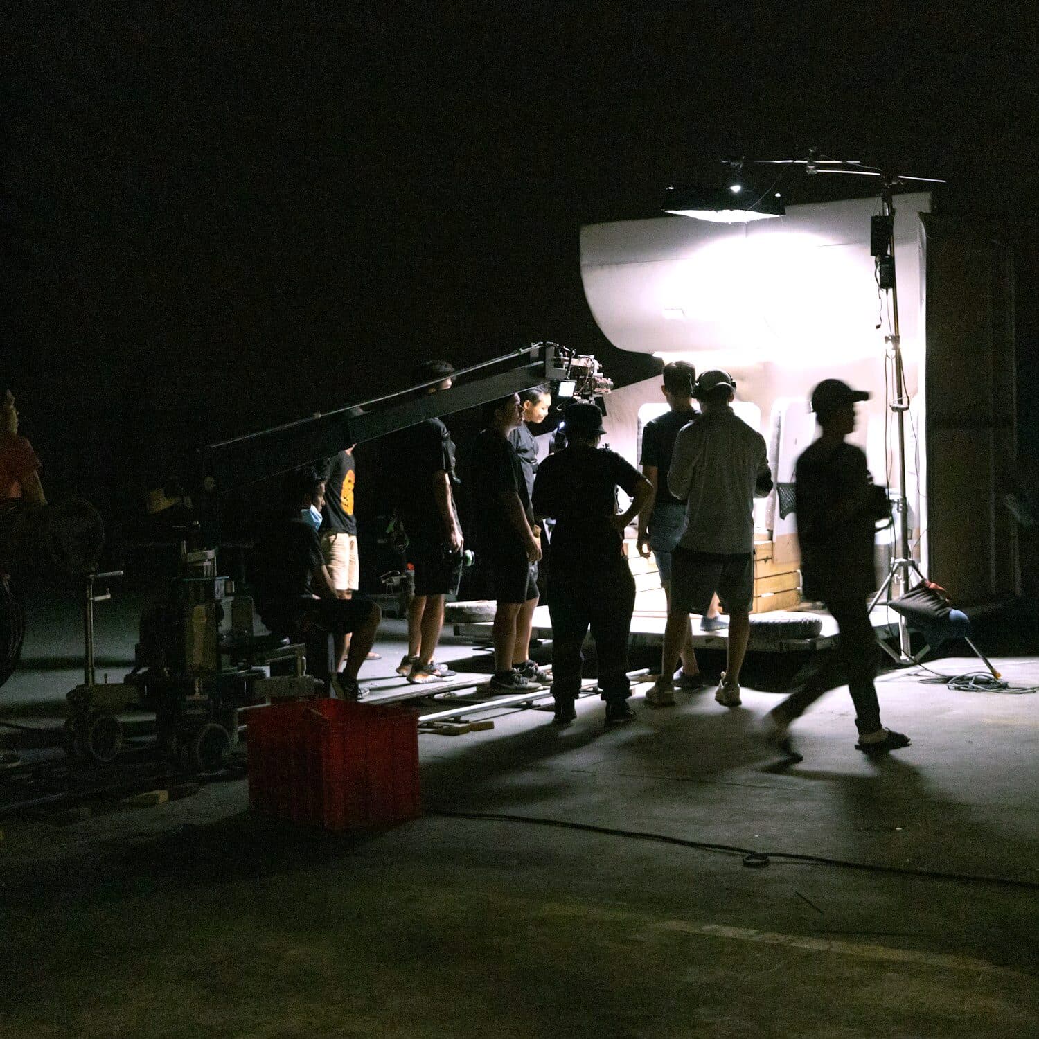 A camera crew at work on a night set, the unit in silhouette against the one light they are shooting by
